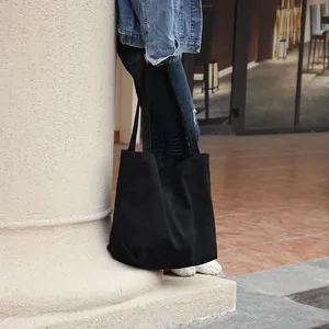 Student in casual denim style carrying a large black canvas tote bag outdoors