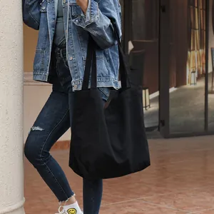 Large minimalist black canvas tote bag shown in a casual urban street lifestyle view