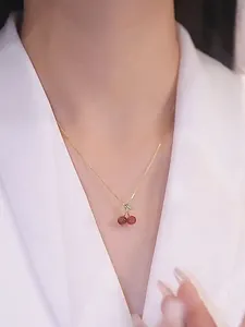 Gros plan d'un élégant collier avec pendentif cerise rouge et chaîne en or sur modèle