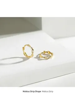 Detailed view of gold Mobius hoop earrings on a minimalist white stone surface.