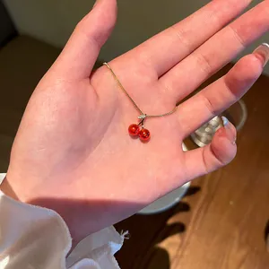 Détail de près d'un collier avec pendentif cerise en argent S925 délicat sur la main