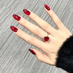 Detailed view of almond-shaped press-on nails with deep red cat-eye effect on hand