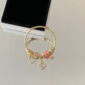 Élégant bracelet à breloques en acier doré avec pierres roses et pendentifs cœur.