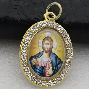 Macro view of a gold-plated oval pendant with inlaid crystals and religious icon.
