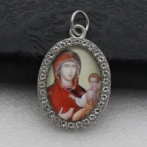 Close-up of an oval rhinestone-encrusted pendant with a religious Saint Mary icon.