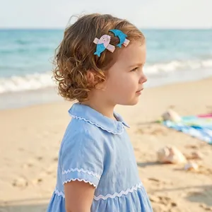 Cute mermaid and dolphin glitter hair clips worn by a little girl on a sunny beach.