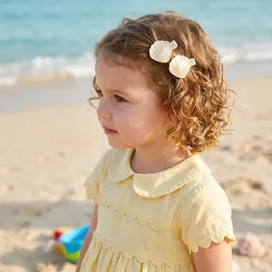 Cute gold shell-shaped hair clips for kids worn by a curly-haired girl on the beach
