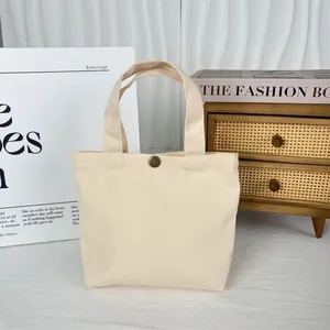 Detailed macro view of cream minimalist canvas tote bag featuring a sturdy metal button closure.