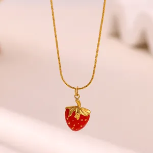 Gros plan d'un pendentif fraise rouge sur une délicate chaîne dorée.