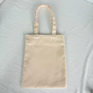 Plain beige canvas tote bag laid flat on a textured white fabric background detail