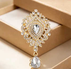Détail d'une broche couronne de luxe avec strass étincelants et pendentif en goutte.