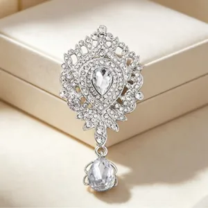 Élégante broche couronne argentée ornée de strass scintillants et d'un cristal en goutte.