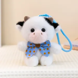 Close-up shot of a cute white plush cow keychain featuring a blue polka dot bow tie