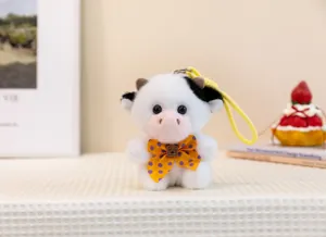 Detailed view of a cute white cow plush keychain featuring a yellow polka-dot bow tie