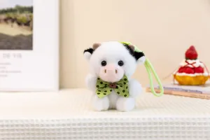 Macro view of a cute white cow plush keychain featuring a green polka-dot bowtie gift
