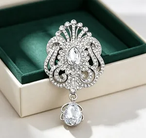 Gros plan d'une élégante broche goutte en strass avec motif couronne en écrin.