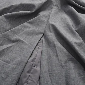 Detail view of grey pleated skirt fabric showing slit and inner lining texture.