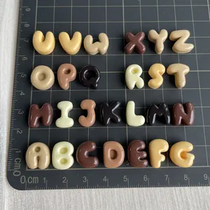 Macro view of 26 small resin alphabet charms in coffee tones on a scale mat.