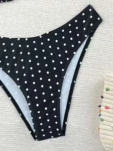 Dettaglio slip bikini nero con stampa a pois bianchi su fondo strutturato.