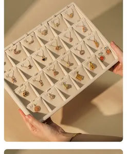 Hands holding a large beige velvet jewelry display tray with various gold necklaces