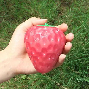 Detail of a large color-changing strawberry squishy toy held in hand in a garden