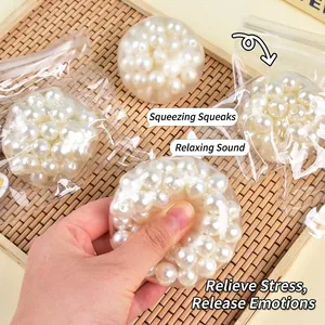 Hand squeezing a pearl-filled clear squishy stress relief toy on a bamboo tray