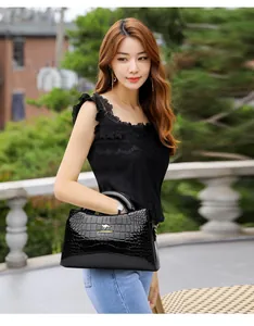 Elegant black crocodile pattern patent leather handbag styled by a model in outdoor setting