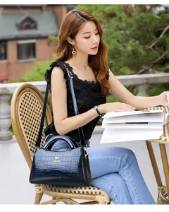 Detail view of blue crocodile embossed patent leather handbag held by a chic model