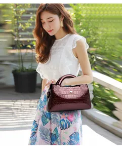 Elegant wine red crocodile-textured patent leather handbag carried by an Asian model