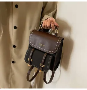 Vintage brown and black leather backpack held by hand against trench coat