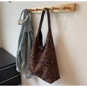 Grande borsa tote scamosciata con stampa leopardata appesa a un gancio a muro in legno.