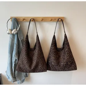 Dettaglio di borse tote in camoscio con stampa leopardata appese a un gancio.