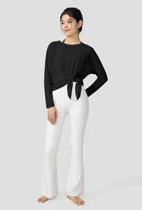Full body view of a woman in a black knotted yoga top and white flared leggings