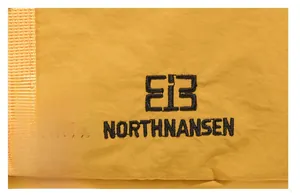 Detailed macro shot of NORTHNANSEN black embroidered logo on yellow backpack fabric