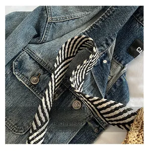 Detail view of a black and white striped strap on a handmade straw woven tote bag.