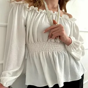 Close-up detail of a white off-the-shoulder blouse with ruffled neckline and smocked waist.