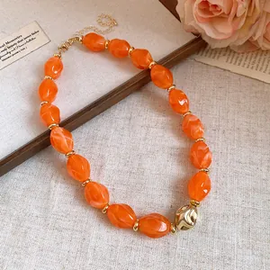 Gros plan d'un collier rétro en acrylique orange avec une perle dorée texturée