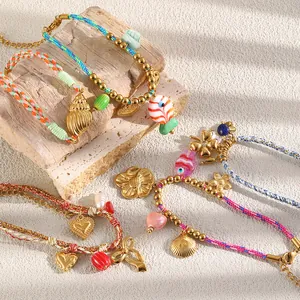 Close-up of colorful woven rope bracelets featuring gold-plated heart, shell, and fish charms