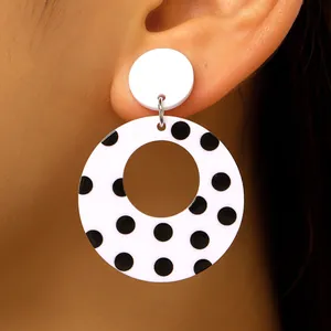 Close-up of large black and white polka dot acrylic hollow hoop earrings on ear.