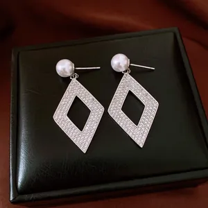 Vista detallada de pendientes de rombo plateados con circonitas y perlas.