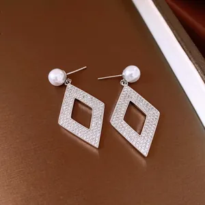 Detalle de cerca de pendientes en forma de rombo hueco con circonitas y perlas