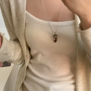 Détail macro d'un collier pendentif grappe de raisin porté sur un pull crème doux