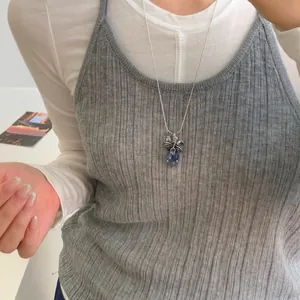 Gros plan d'un collier pendentif grappe de raisin porté sur un débardeur gris côtelé