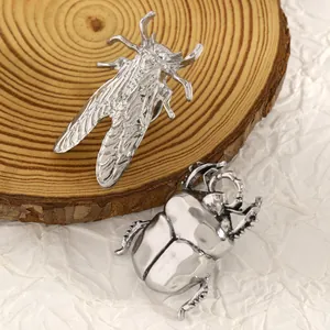 Dettaglio di spille a forma di cicala e scarabeo in argento su un disco di legno