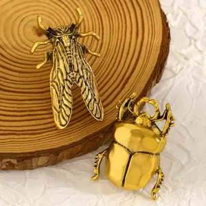 Primo piano di spille a forma di cicala e scarabeo in oro vintage su sfondo di legno