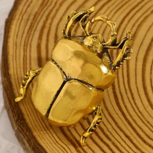 Dettaglio di una spilla a scarabeo dorata vintage con texture metallica su legno