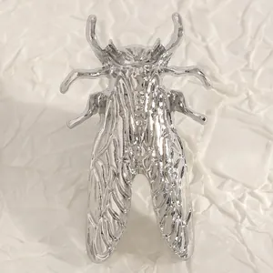 Dettaglio macro di una spilla a forma di cicala d'argento con trame metalliche.