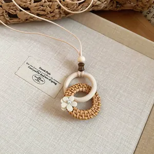 Detailed view of a bohemian rattan woven pendant necklace with wooden ring and flower.