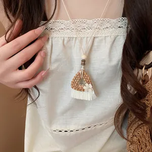Close-up of handmade rattan triangle pendant necklace with white flower and fringe.