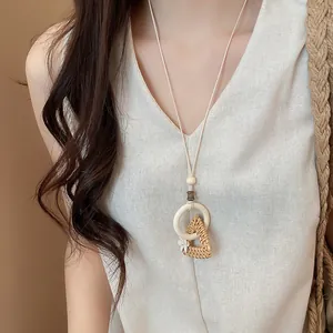 Detailed view of a handmade woven rattan pendant necklace worn with minimalist linen clothing